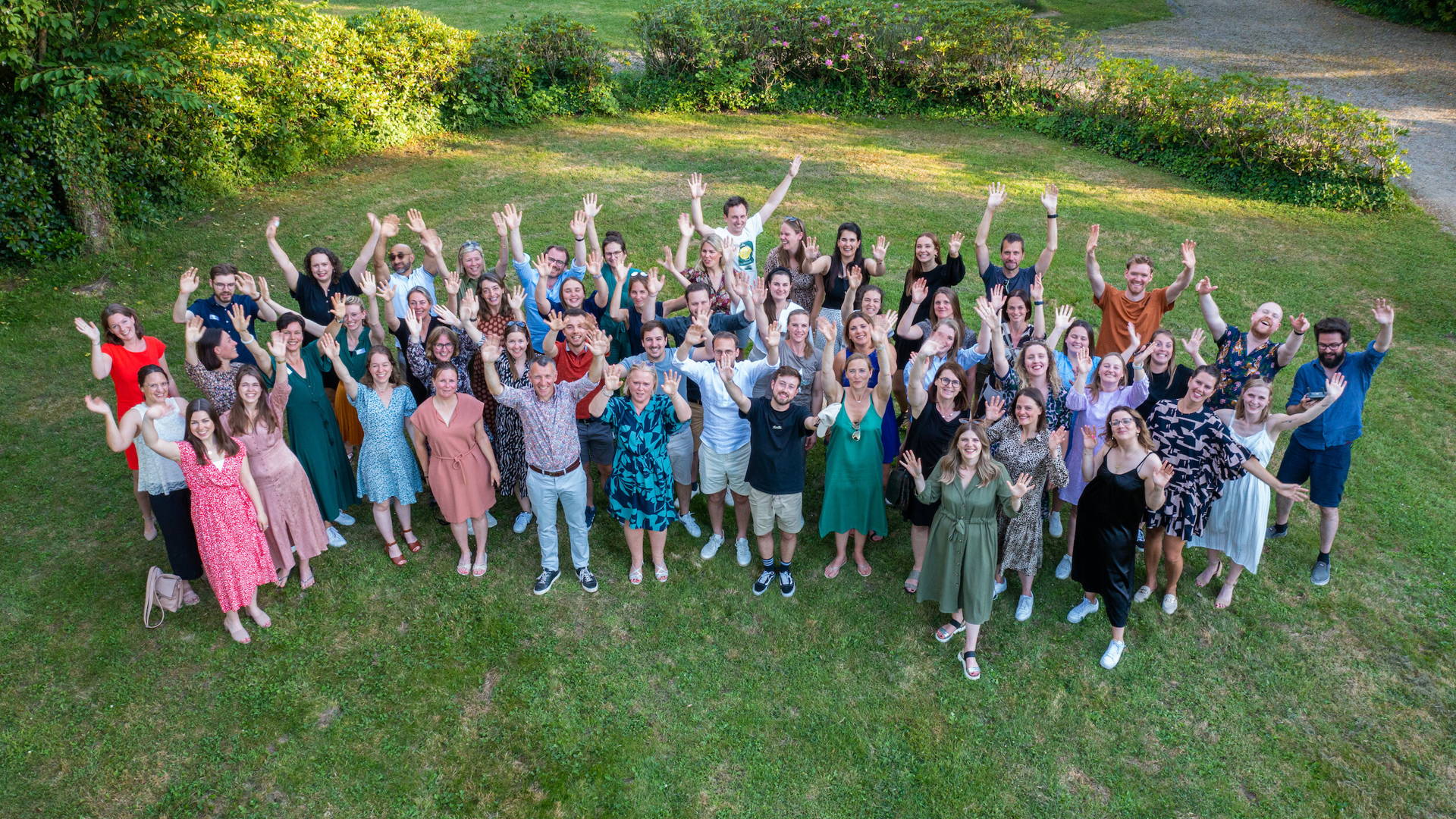 Groepsfoto van alle medewerkers van Connect. Ze staan op gras en houden de armen in de lucht.