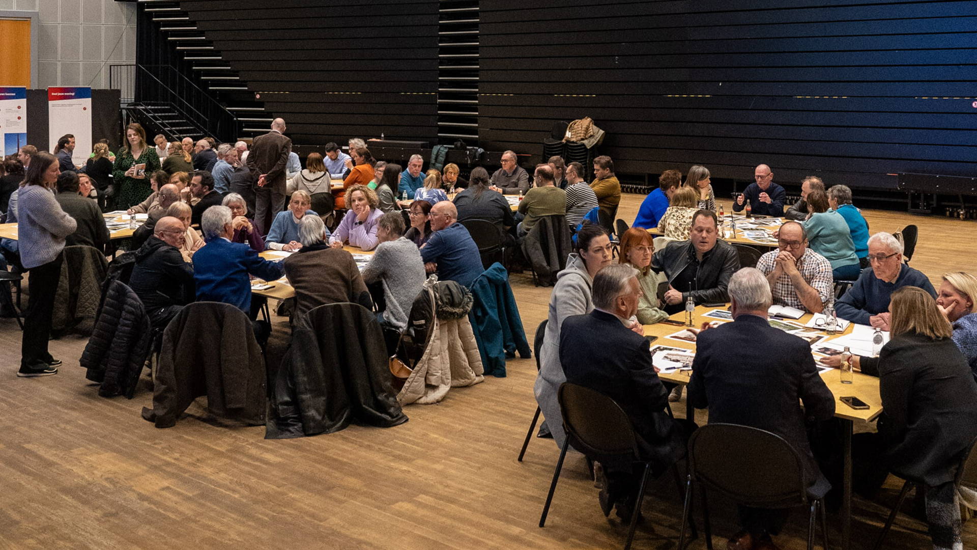 Themacafé Stad Borgloon. Bezoekers met elkaar in gesprek over het project. Verschillende groepen aan aparte tafels.