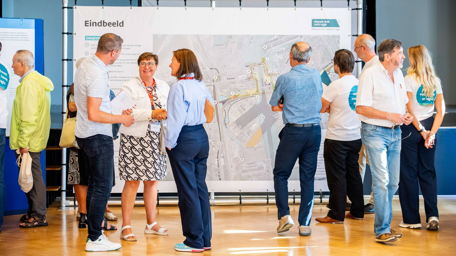 Vue générale d'une salle lors d'une séance d'information du projet Nieuwe Sluis Zeebrugge. Les visiteurs discutent avec les membres de l'équipe projet.