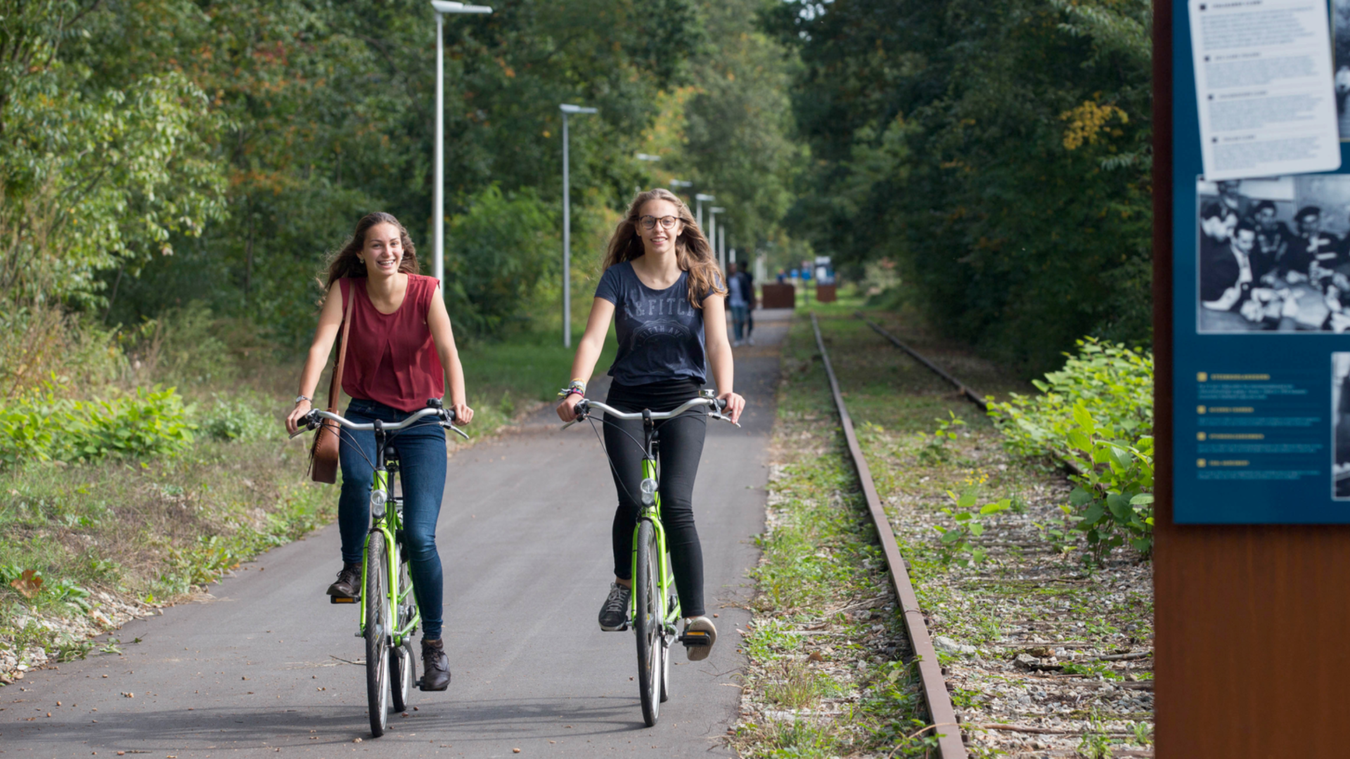 Projet Kolenspoor: deux cyclistes vues de face roulent à vélo à côté d'une voie de chemin de fer désaffectée.