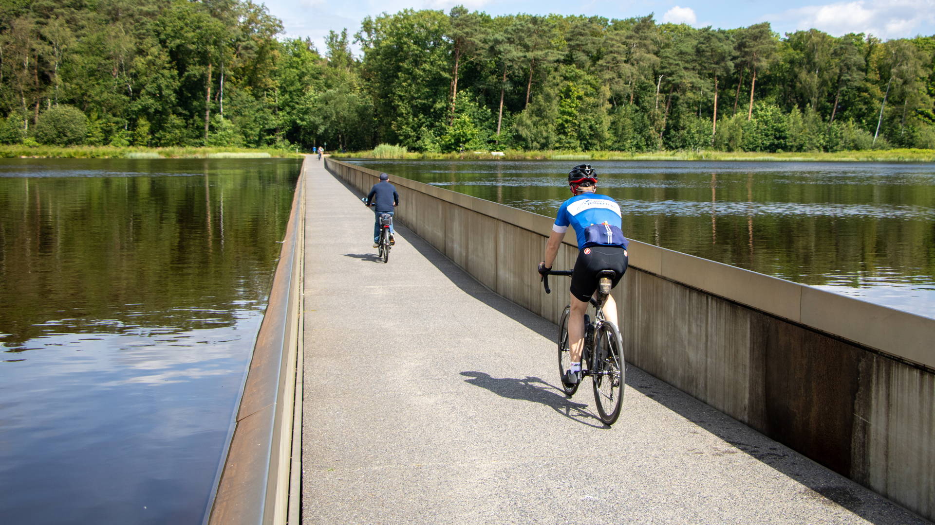 Projet Kolenspoor: des cyclistes roulent sur piste cyclable au milieu d'un plan d'eau.