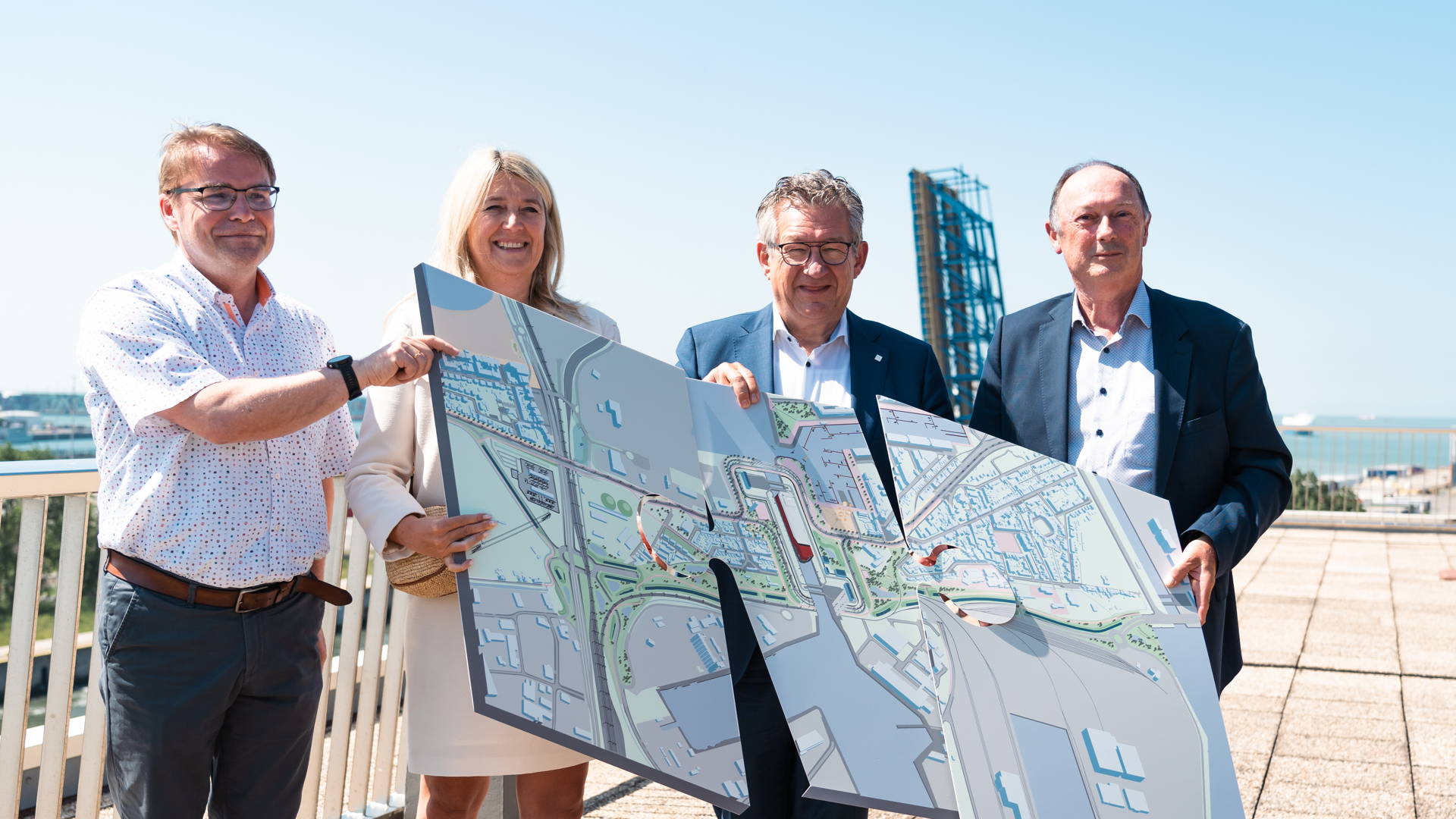 Les partenaires du projet Nieuwe Sluis Zeebrugge posent avec des pièces de puzzle géantes présentant le futur projet. La photo est prise avec l'écluse actuelle en arrière-plan.