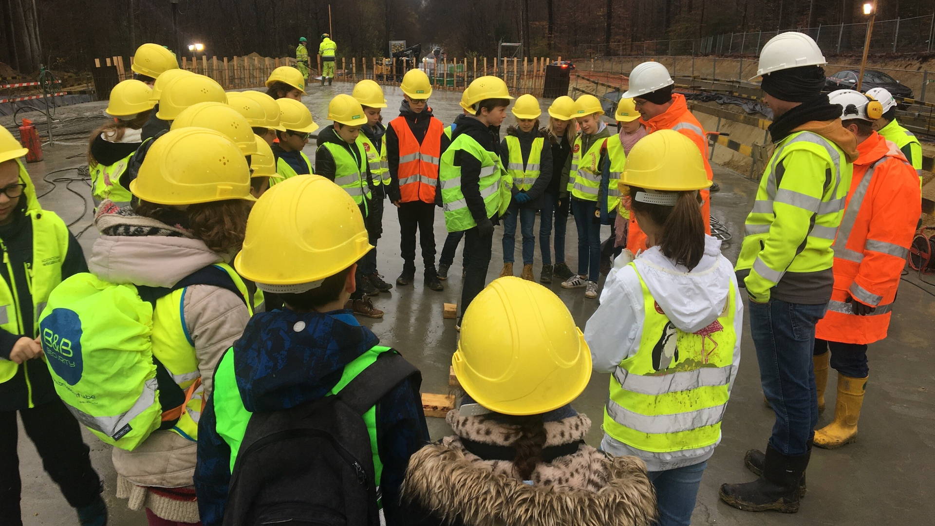 AWV werfbezoek. Leerlingen in werkkledij (helm, fluovest) brengen een bezoek aan de AWV werf.